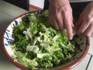 tossing frisee lettuce in a bowl