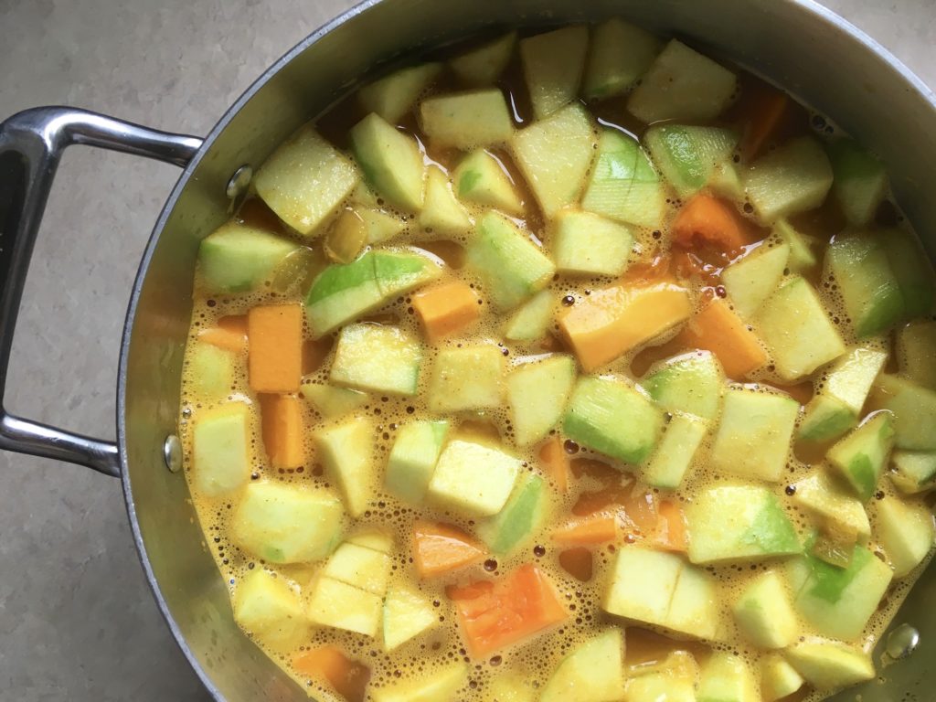 chopped apples and butternut squash simmering in vegetable stock in pot