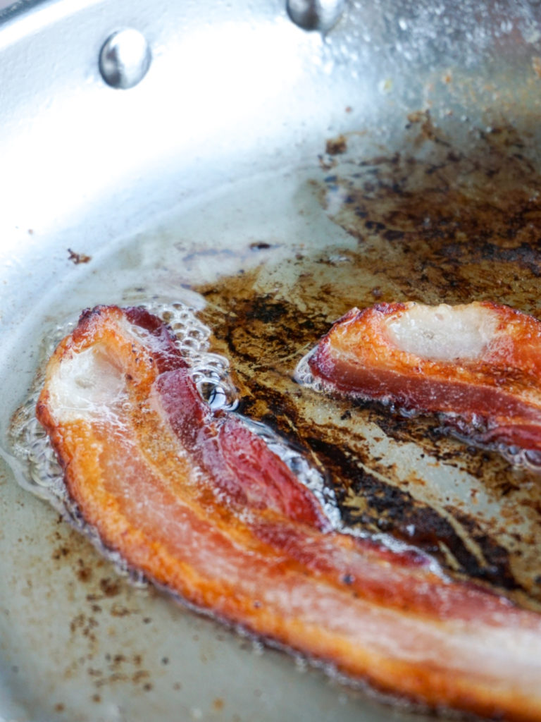 Bacon frying in stainless steel pan for orecchiette with kale, bacon, and sun-dried tomatoes