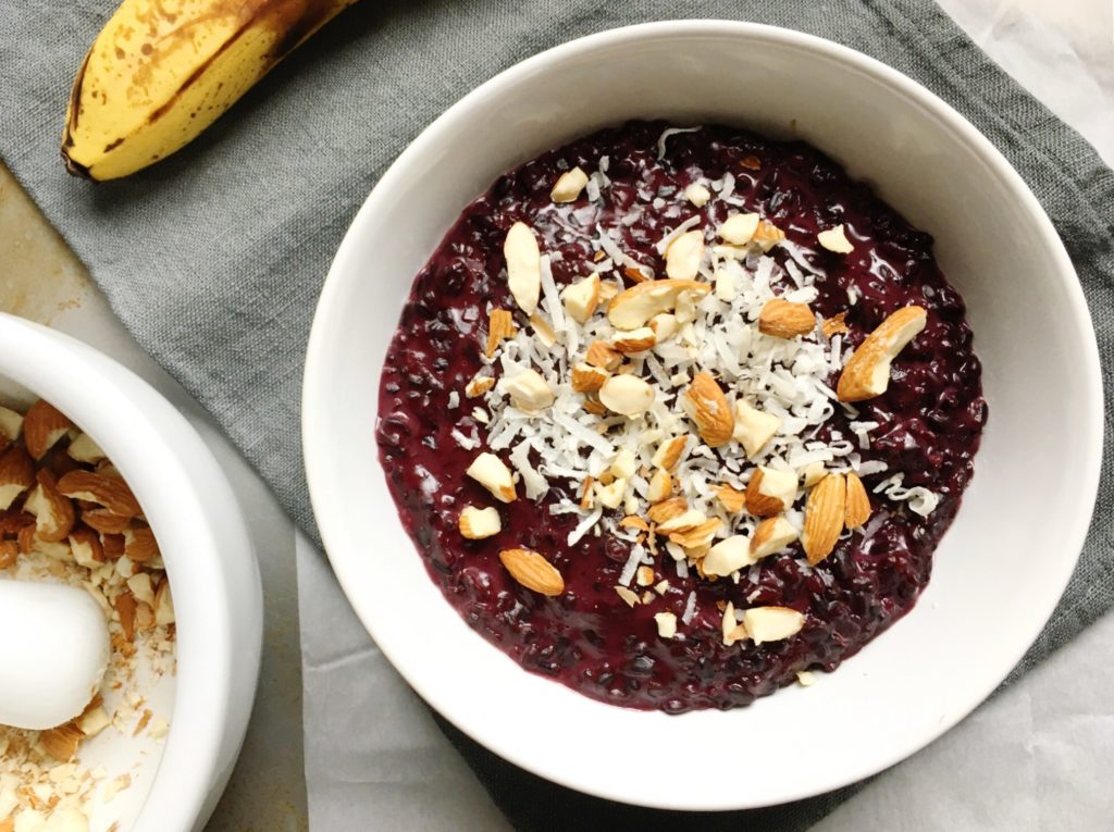 Bowl of coconut black rice breakfast porridge on linen napkin topped with shredded coconut and almonds