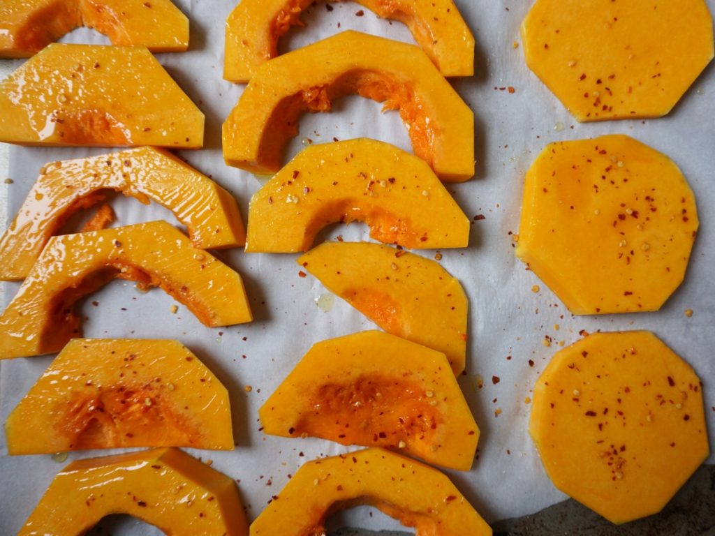 Sliced butternut squash on baking sheet with olive oil and red pepper flakes