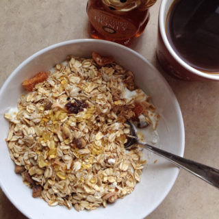bowl of yogurt topped with muesli with nuts, dried fruit, and coconut, with honey and coffee