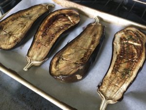 Two eggplants, halved, scored, and roasted, on a baking sheet coming out of the oven