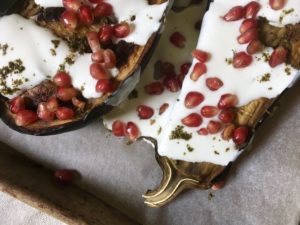 The top of one and the bottom of another eggplant, dressed in greek yogurt and buttermilk dressing with pomegranate seeds on top