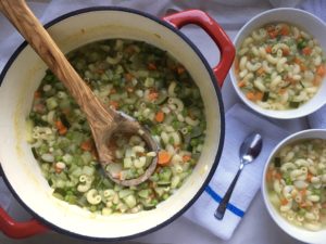 French bean and pasta soup in red dutch oven with olive wood ladle and two full bowls to the right