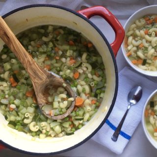 French bean and pasta soup in red dutch oven with olive wood ladle and two full bowls to the right