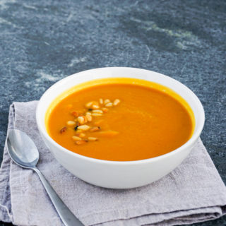 Curried butternut squash and apple soup in white bowl on grey marble background