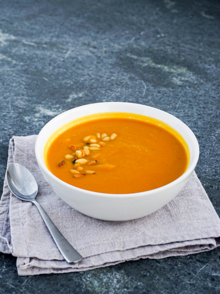 Curried butternut squash and apple soup in white bowl on grey marble background