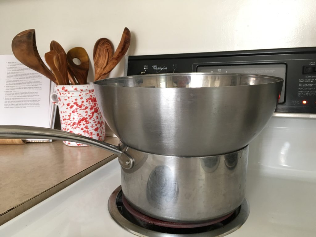 Stainless steel bowl set on top of a pot of simmering water, with splattered puglia utensil holder in the background