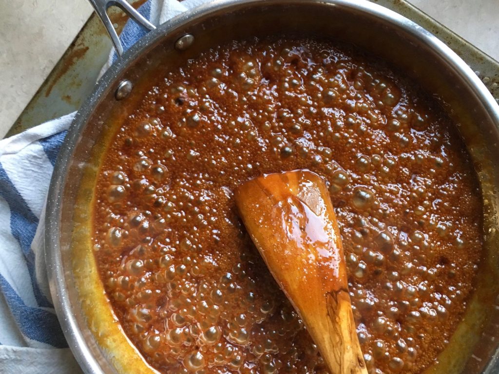 David Lebovitz's salted caramel sauce boiling in a pan, being stirred by a flat olive wood spatula