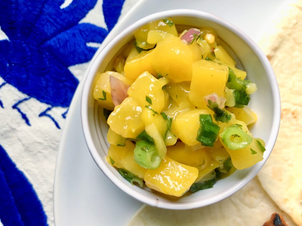 Mango salsa with lime, cilantro, and green onions in white bowl on blue Otomi background