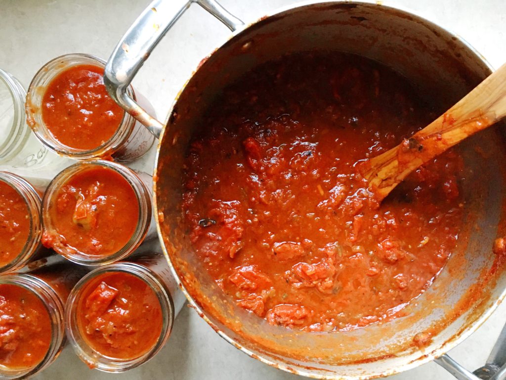 Bold marinara sauce in pot and in six canning jars