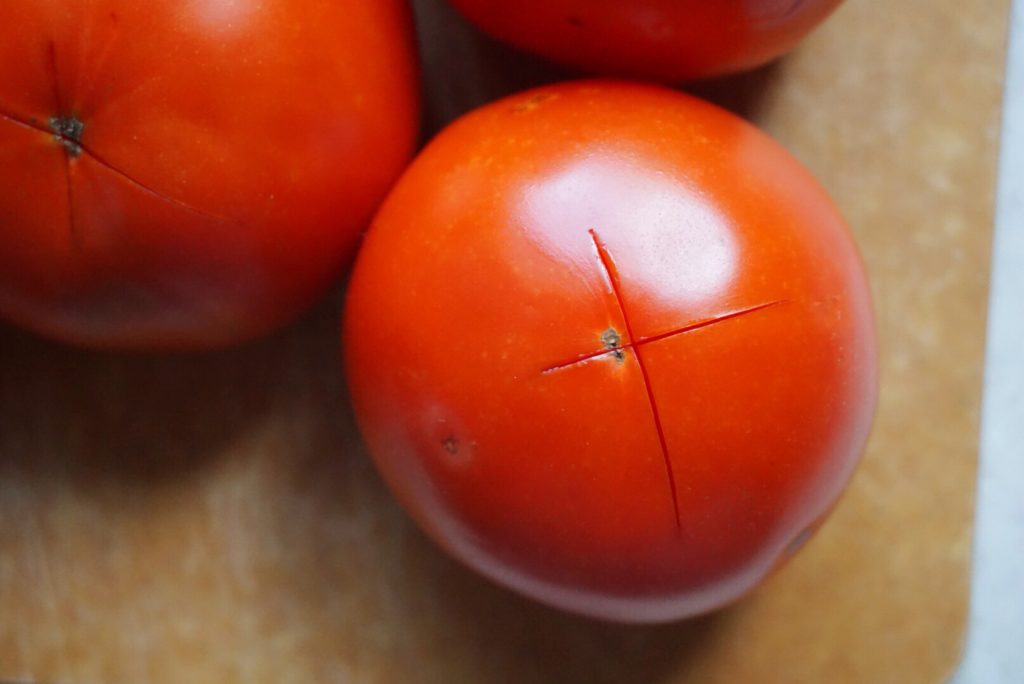 Early Girl tomatoes, scored with an x on epicurean cutting board