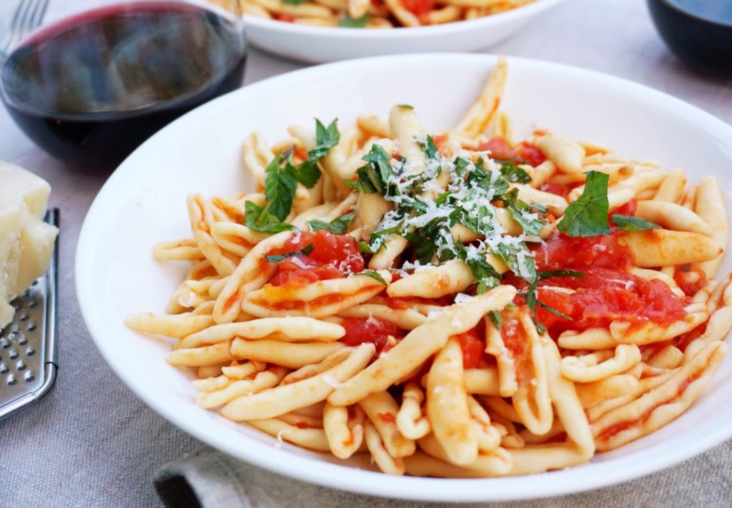 Pasta al Pomodoro on white deep plate with wine and parmesan cheese