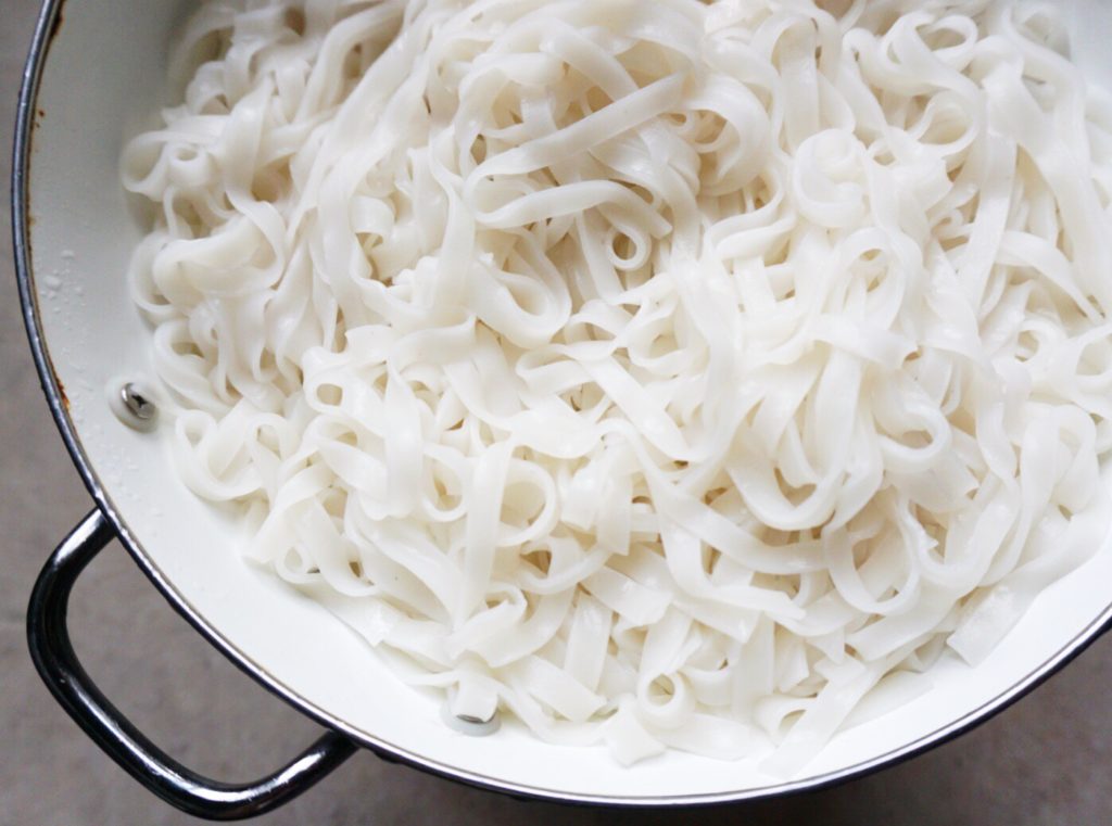 Cooked banh pho noodles for pad thai draining in colander for homemade pad thai recipe