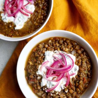 Two bowls of Slow Cooker Dal with Quick-Pickled Onions and Cilantro-Yogurt Dollop recipe on yellow linen background