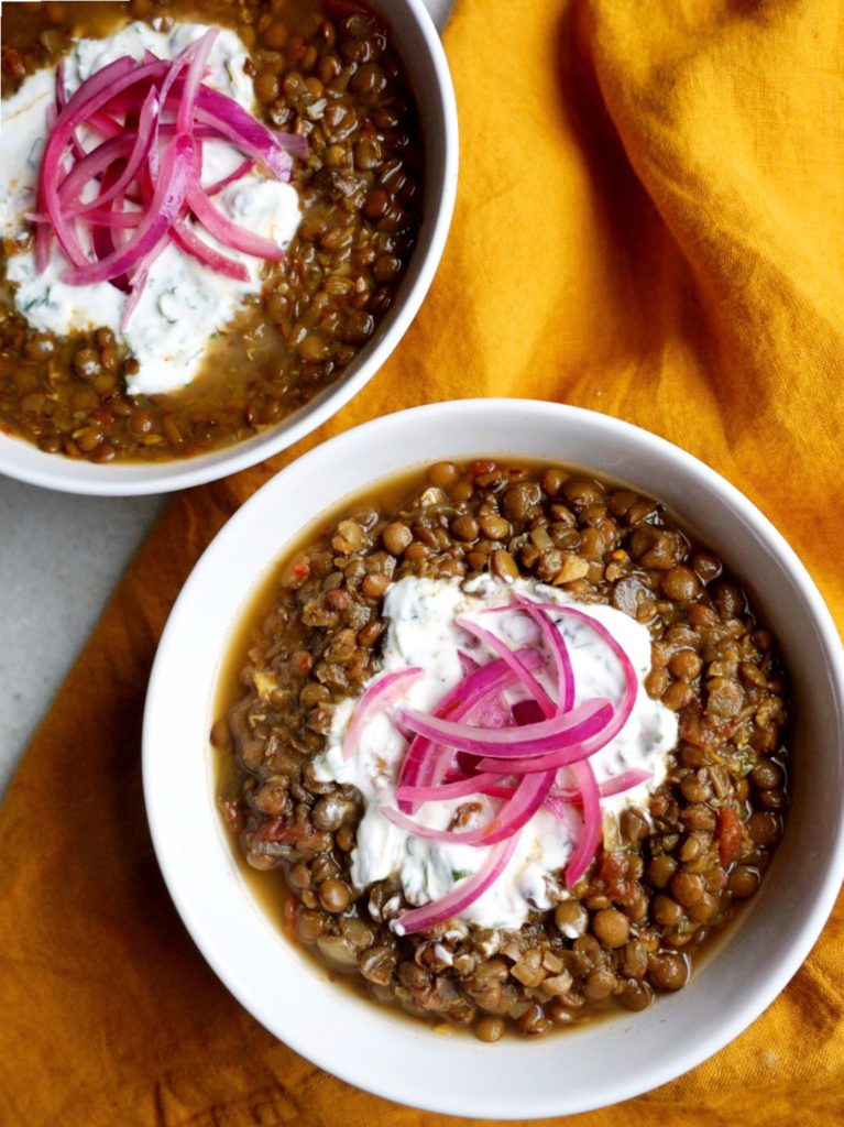 Two bowls of Slow Cooker Dal with Quick-Pickled Onions and Cilantro-Yogurt Dollop recipe on yellow linen background