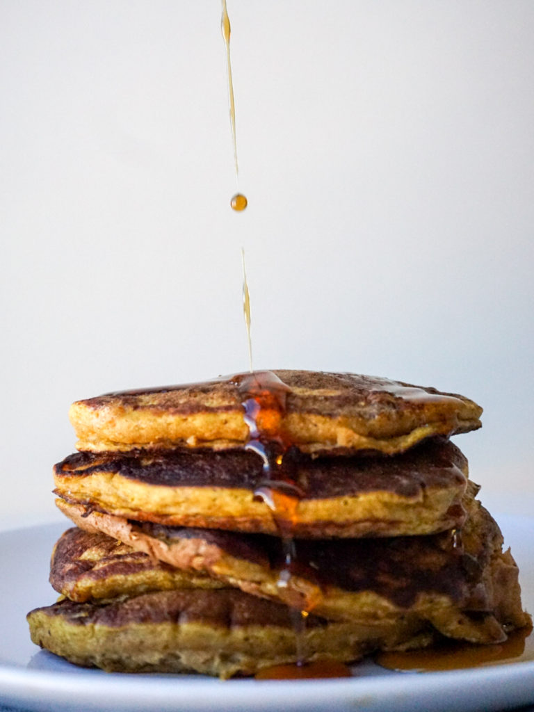 Homemade pumpkin pancake recipe topped with maple syrup on white plate