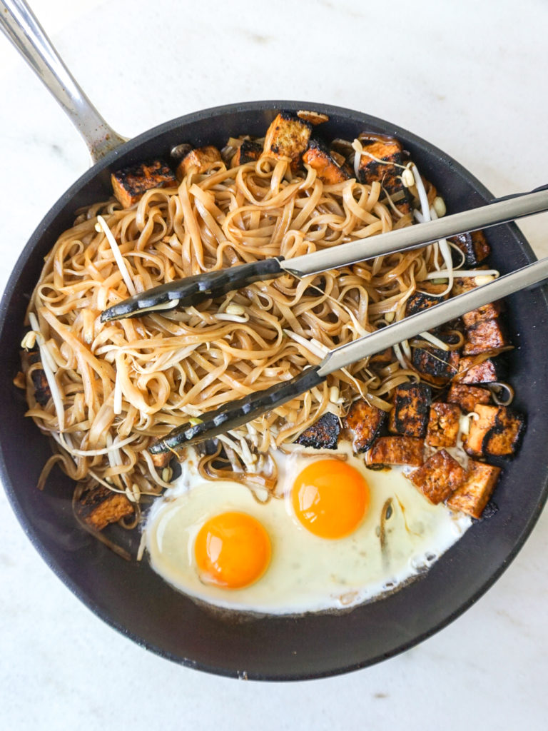 Eggs, tofu, noodles, and beansprouts frying in pan for homemade pad thai recipe