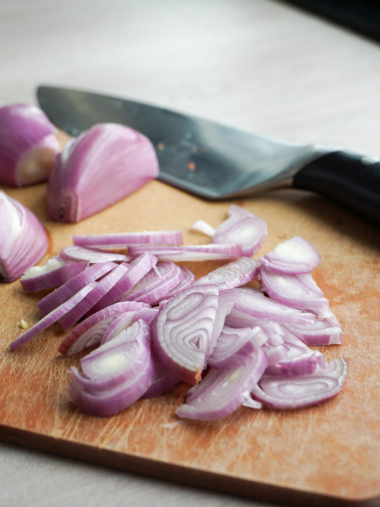 Slice shallots on cutting board for halibut recipe