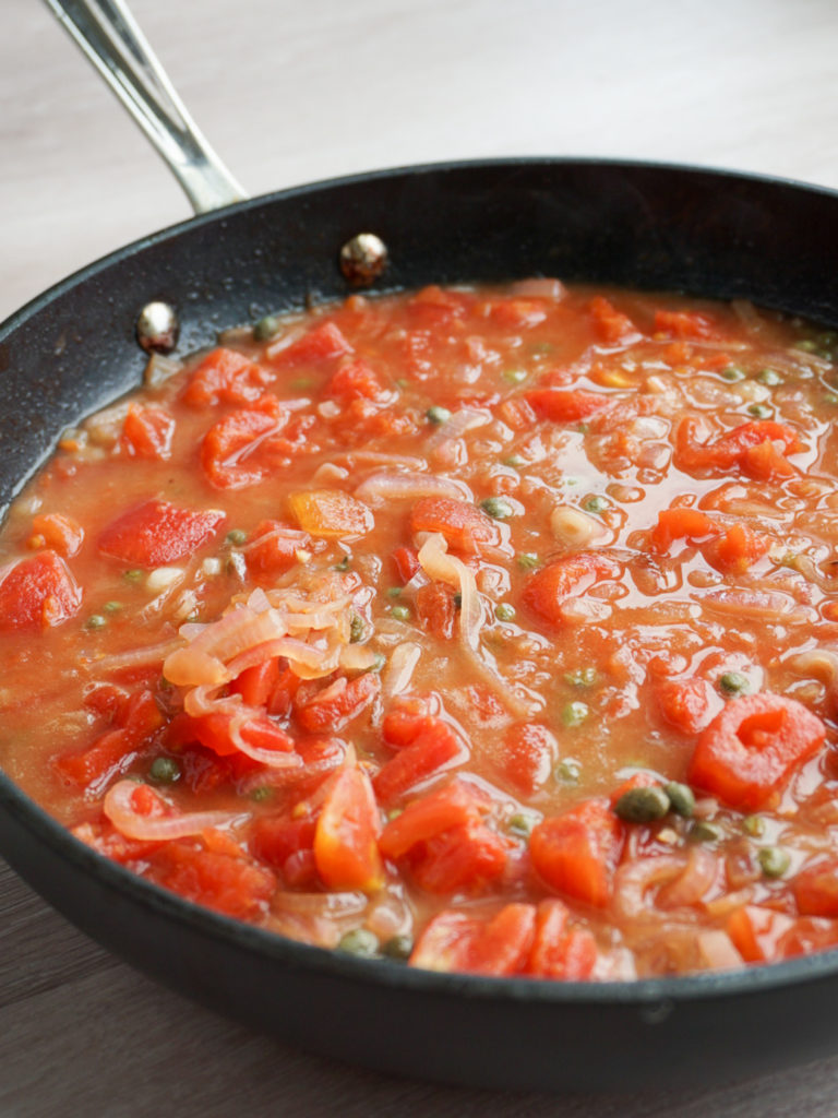 White wine, butter, tomato, lemon, and caper sauce in pan for seared halibut recipe