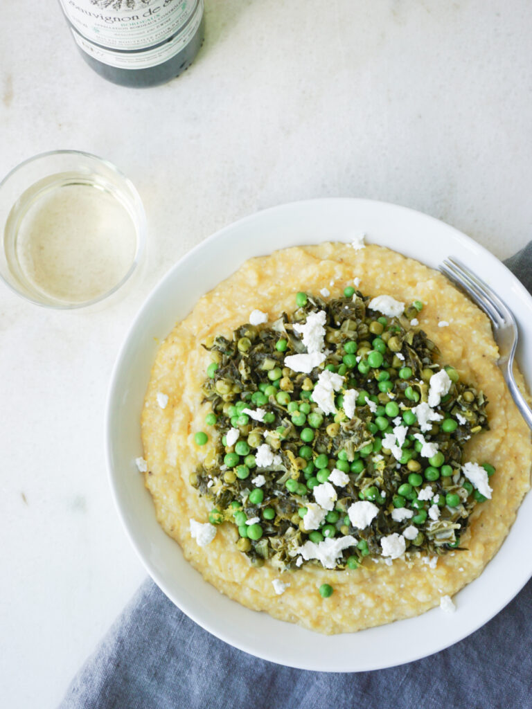 Healthy polenta recipe with spinach, peas, and goat cheese in white dish with white wine